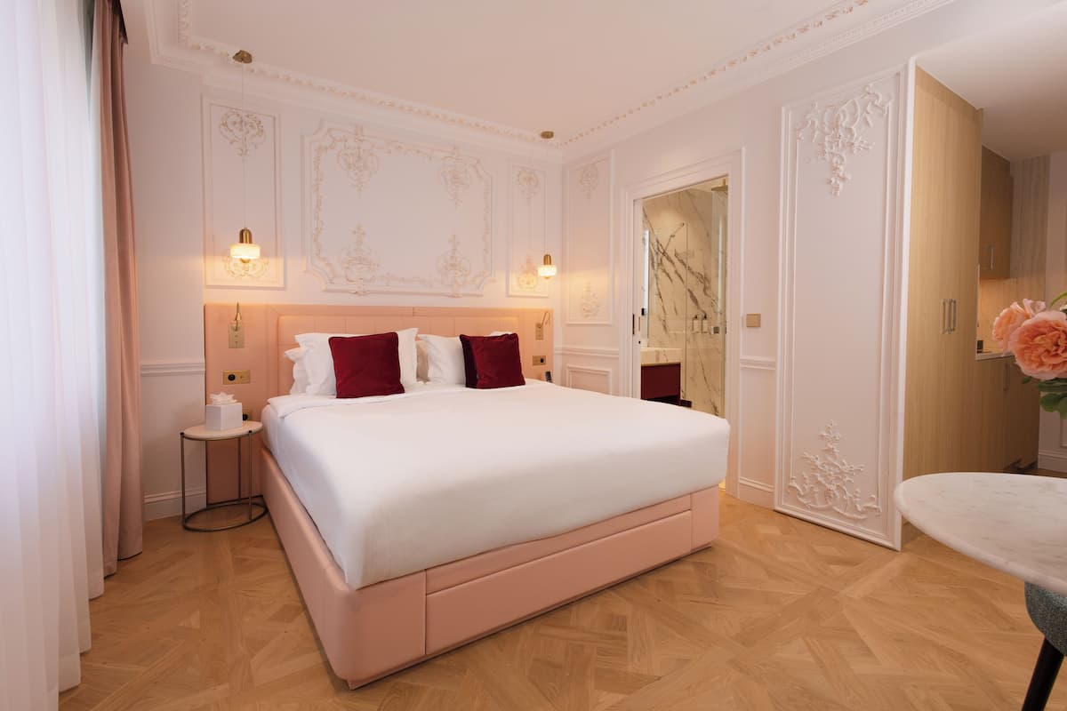 A hotel room with a large bed, a bedside table, a nightstand, and a bathroom visible through an open door.