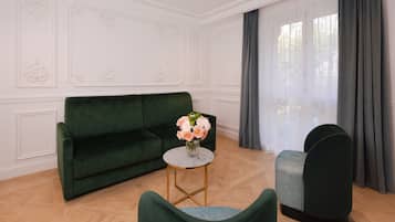 Una habitación con un sofá verde, una mesa redonda con un florero y un sillón verde.