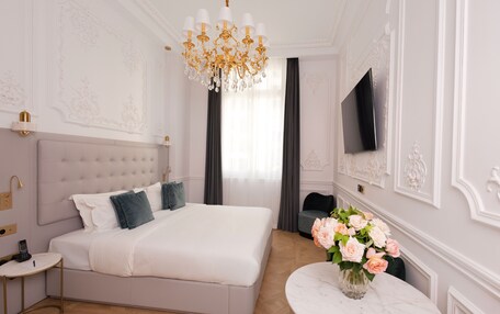 A bedroom with a large bed, a television on the wall, a chandelier, and a vase with flowers on a table.