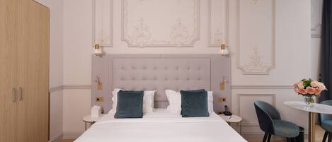 A hotel room with a large bed, a round table with chairs, and a chandelier.
