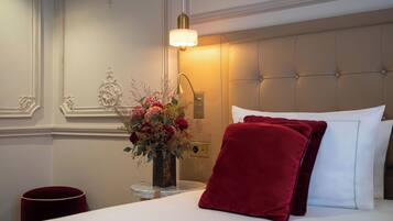 A hotel room with a bed, a vase of flowers, a lamp, and a red pillow.