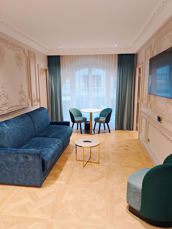 Un salón moderno con un sofá azul, dos sillones verdes, una mesita redonda y un televisor montado en la pared.