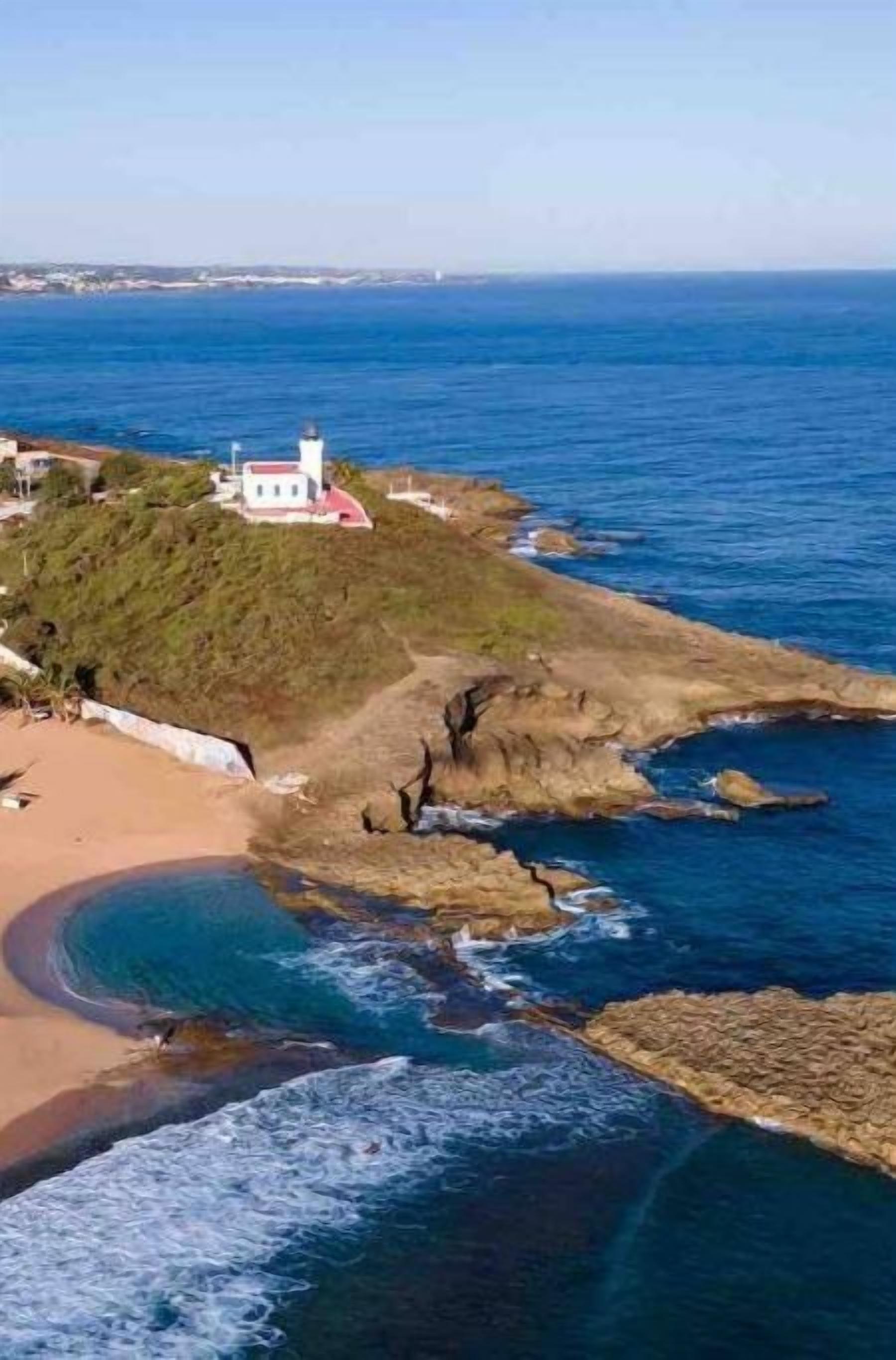 A coastal view with a lighthouse, beach, and rocky shoreline.