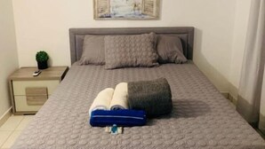 Een slaapkamer met een bed, een nachtkastje, een kleine plant en een schilderij aan de muur.