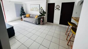 Een ruime woonkamer met een bank, een kleine kerstboom en een eettafel met stoelen.