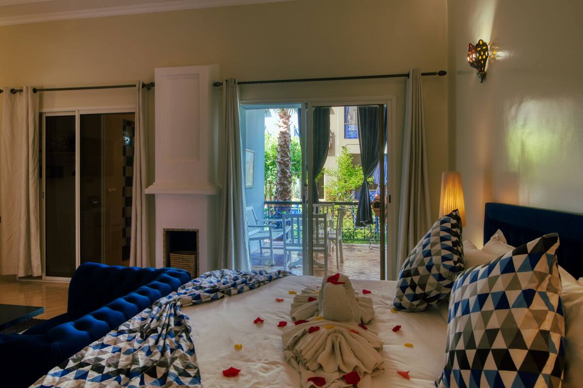 Une chambre d’hôtel avec un lit, un canapé bleu, une cheminée et une vue sur la terrasse extérieure.