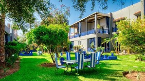 Un patio con zona de comedor, rodeado de abundante vegetación y un edificio con balcones.