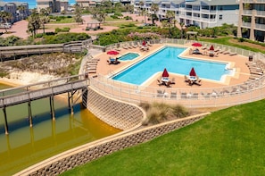 A resort with a large pool, lounge chairs, and a bridge over a water feature.