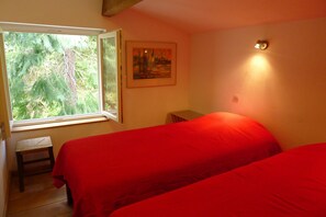 A bedroom with two beds, a window with a view of trees, a painting on the wall, and a small stool. - The River Mountain House at 1,000m altitude in the Pyrenées-Orièntales (Nohèdes)