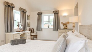 A bedroom with a bed, a dresser, a vanity with a mirror, and a window with curtains.