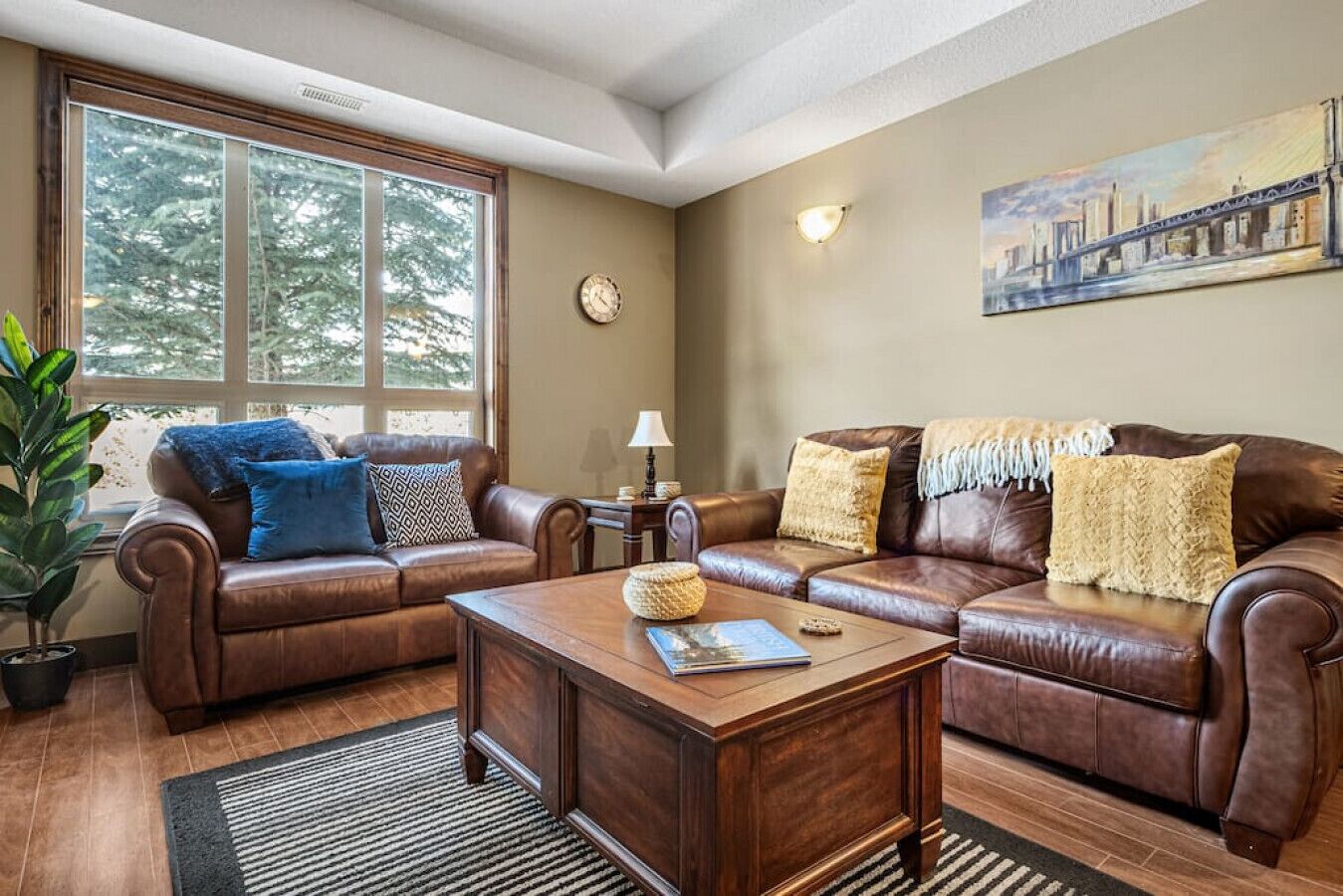A living room with two brown leather sofas, a wooden coffee table, and a large window with a view of trees.