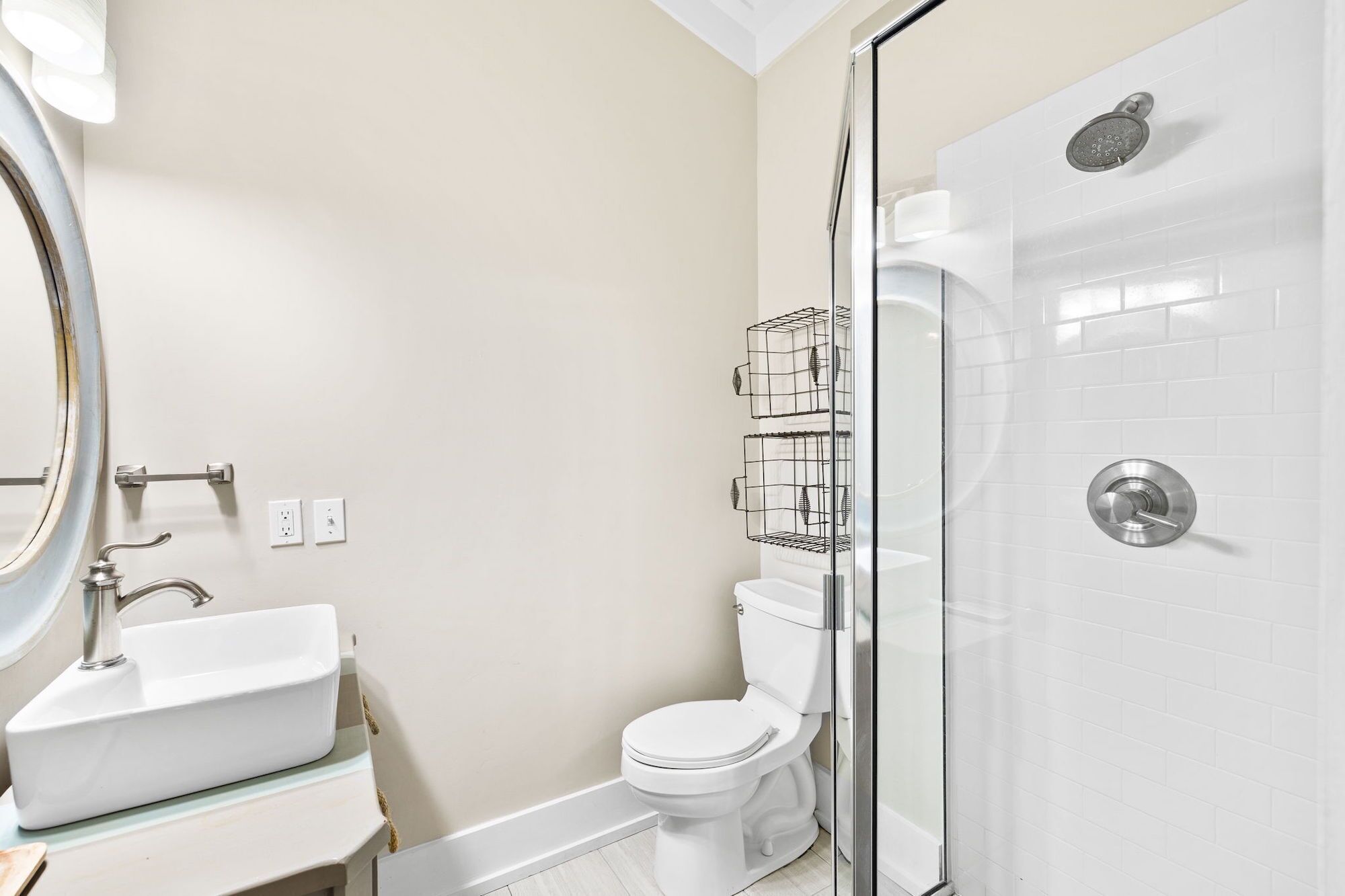 Une salle de bain avec un lavabo, des toilettes et une douche, le tout de couleur blanche. La douche est séparée par une porte en verre, et un porte-serviettes en métal est fixé au-dessus des toilettes.