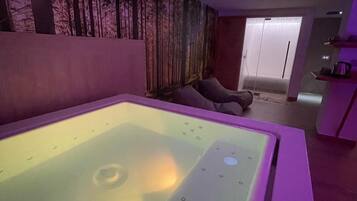 Ein Zimmer mit einer großen, beheizten Badewanne, einer Wand mit einem Waldfries und einer Tür zu einem weiteren Raum.