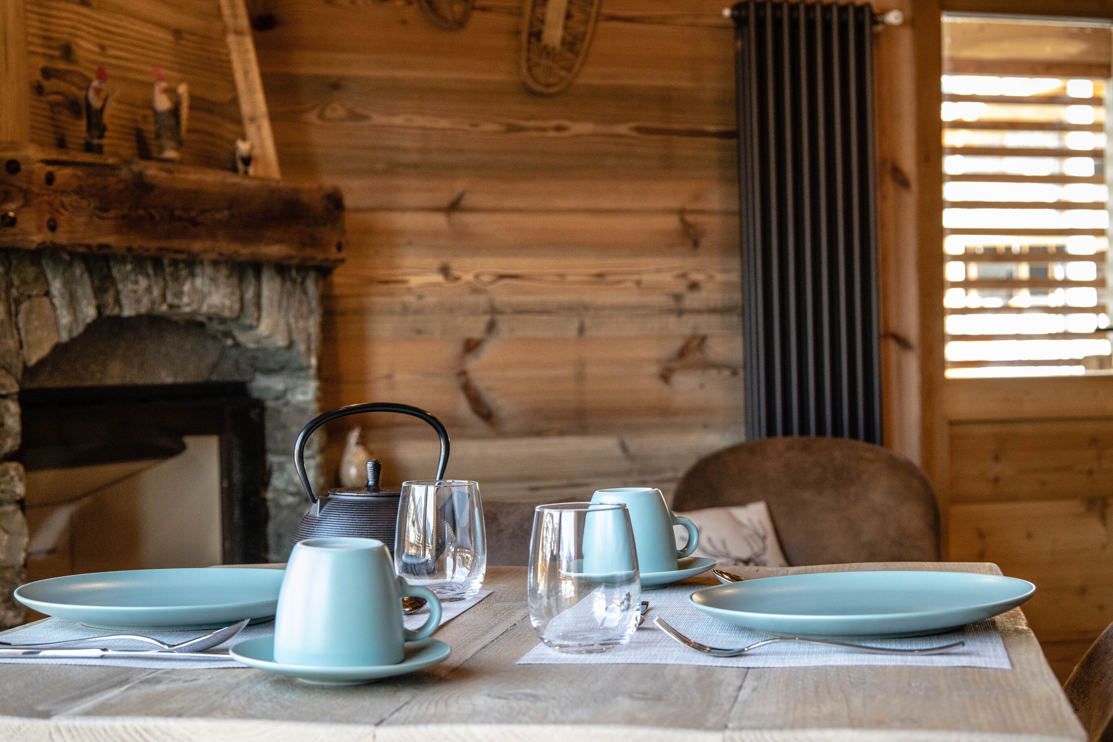 A wooden interior with a fireplace, a table set with blue plates, cups, and glasses, and a chair.