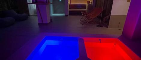 A room with two heated pools, a seating area, and a doorway leading to another room.