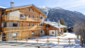Een meerlaags houten lodge met balkons, stenen muren en een berg in de achtergrond bedekt met sneeuw.