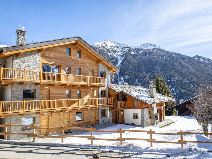 Een meerlaags houten lodge met balkons, stenen muren en een berg in de achtergrond bedekt met sneeuw.