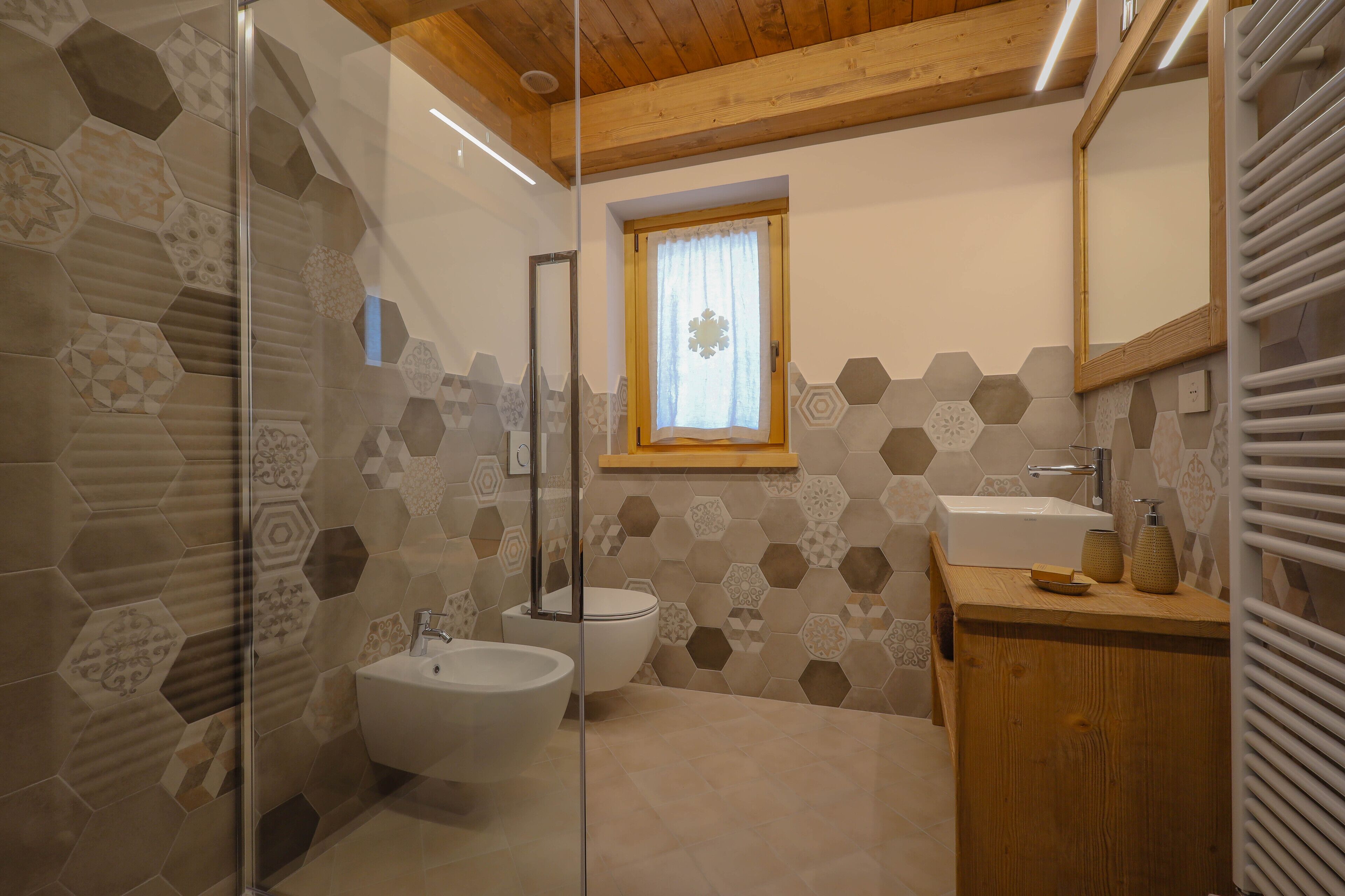 A bathroom with a glass shower enclosure, a white sink, a bidet, and a wooden vanity.
