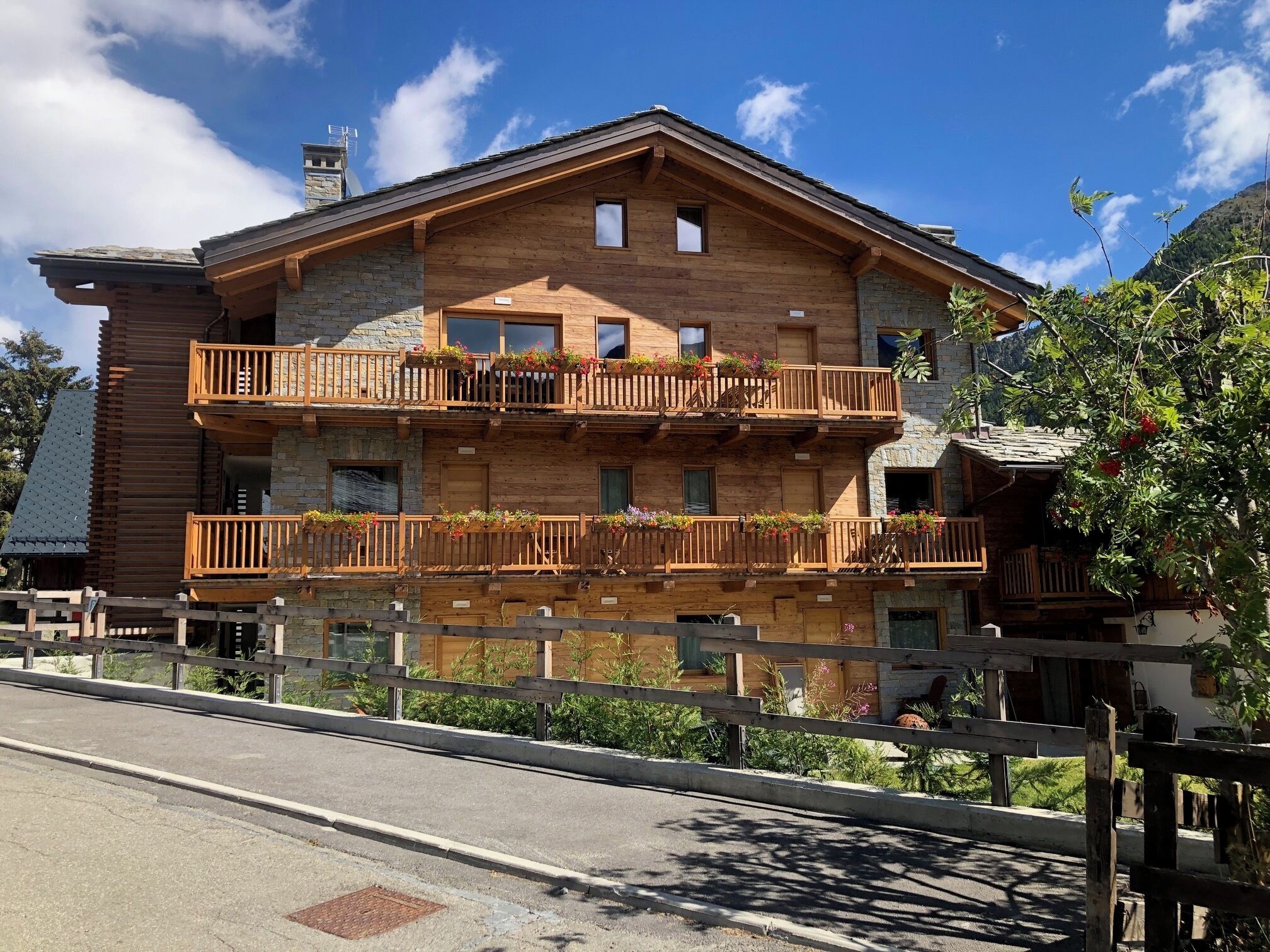 Eine zweistöckige Holzchalet mit Balkonen, Steinverzierungen und Blick auf die umliegende Landschaft.