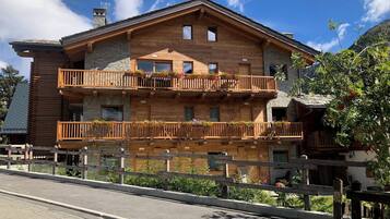 Eine zweistöckige Holzchalet mit Balkonen, Steinverzierungen und Blick auf die umliegende Landschaft.