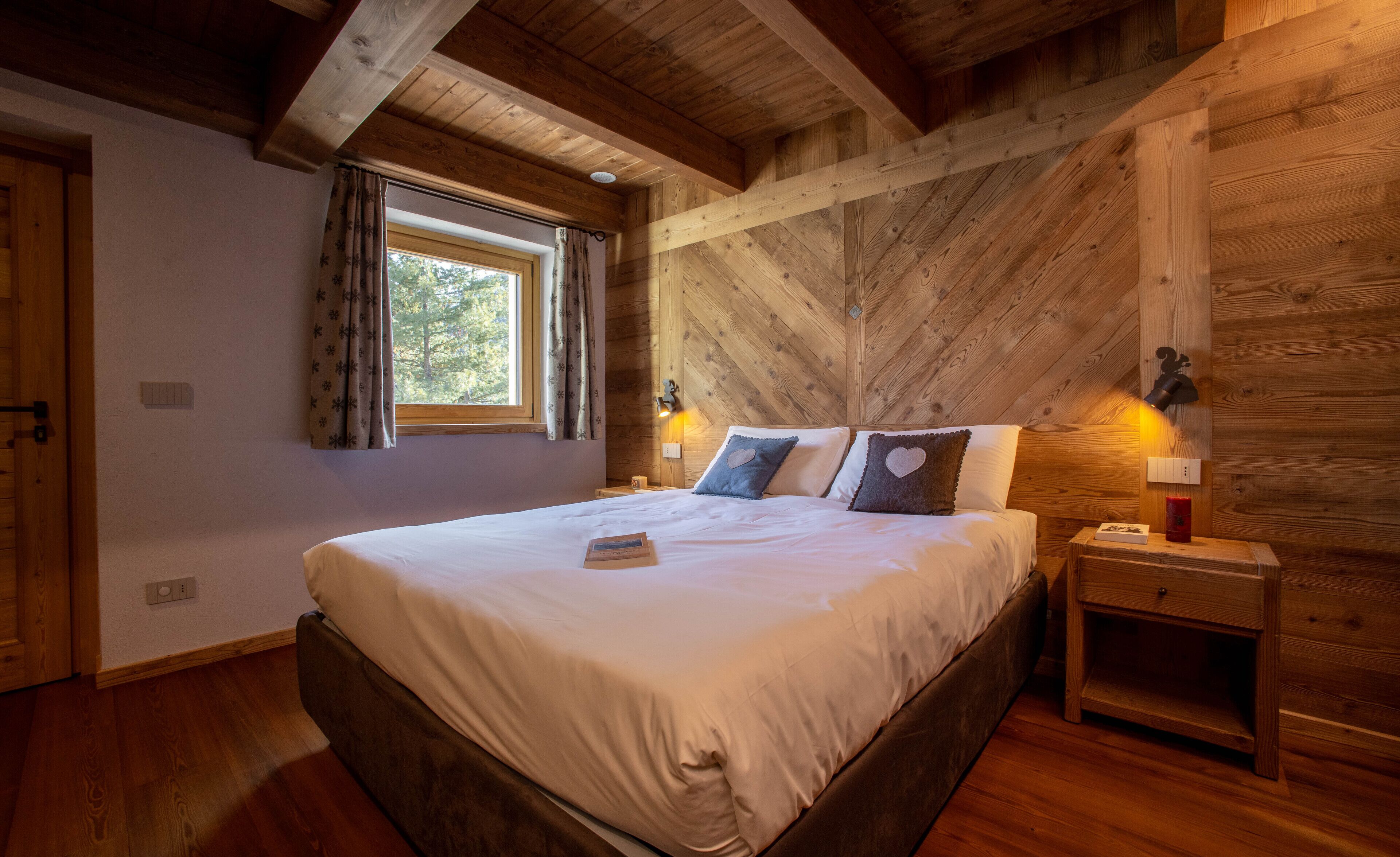 Ein Schlafzimmer mit Holzboden, einem großen Bett mit weißer Bettwäsche, zwei Nachttischlampen und einem Fenster mit Vorhängen.