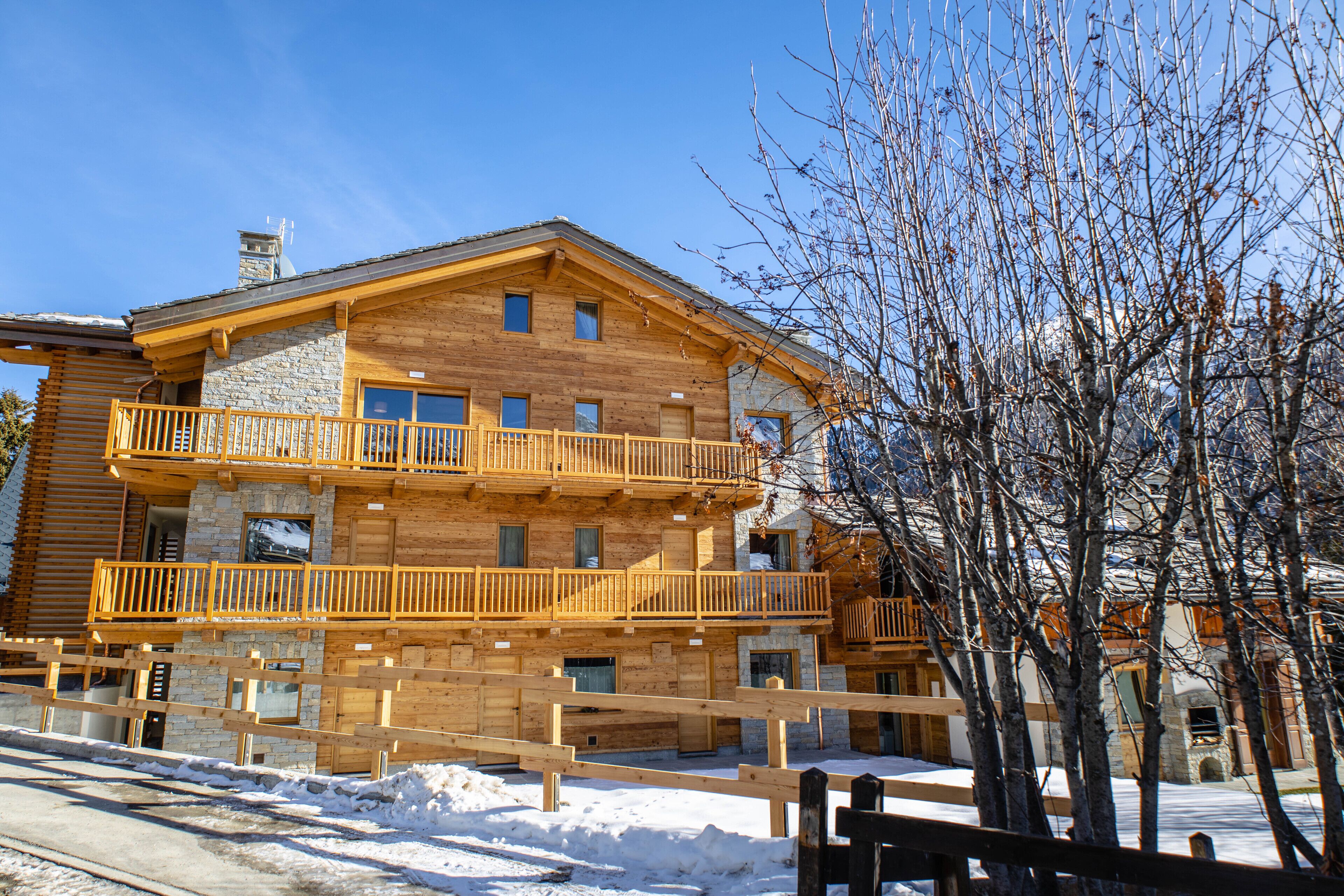 Un immeuble en bois à plusieurs étages, doté de balcons, d’une façade en pierre et d’un sol recouvert de neige.