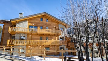 Un immeuble en bois à plusieurs étages, doté de balcons, d’une façade en pierre et d’un sol recouvert de neige.