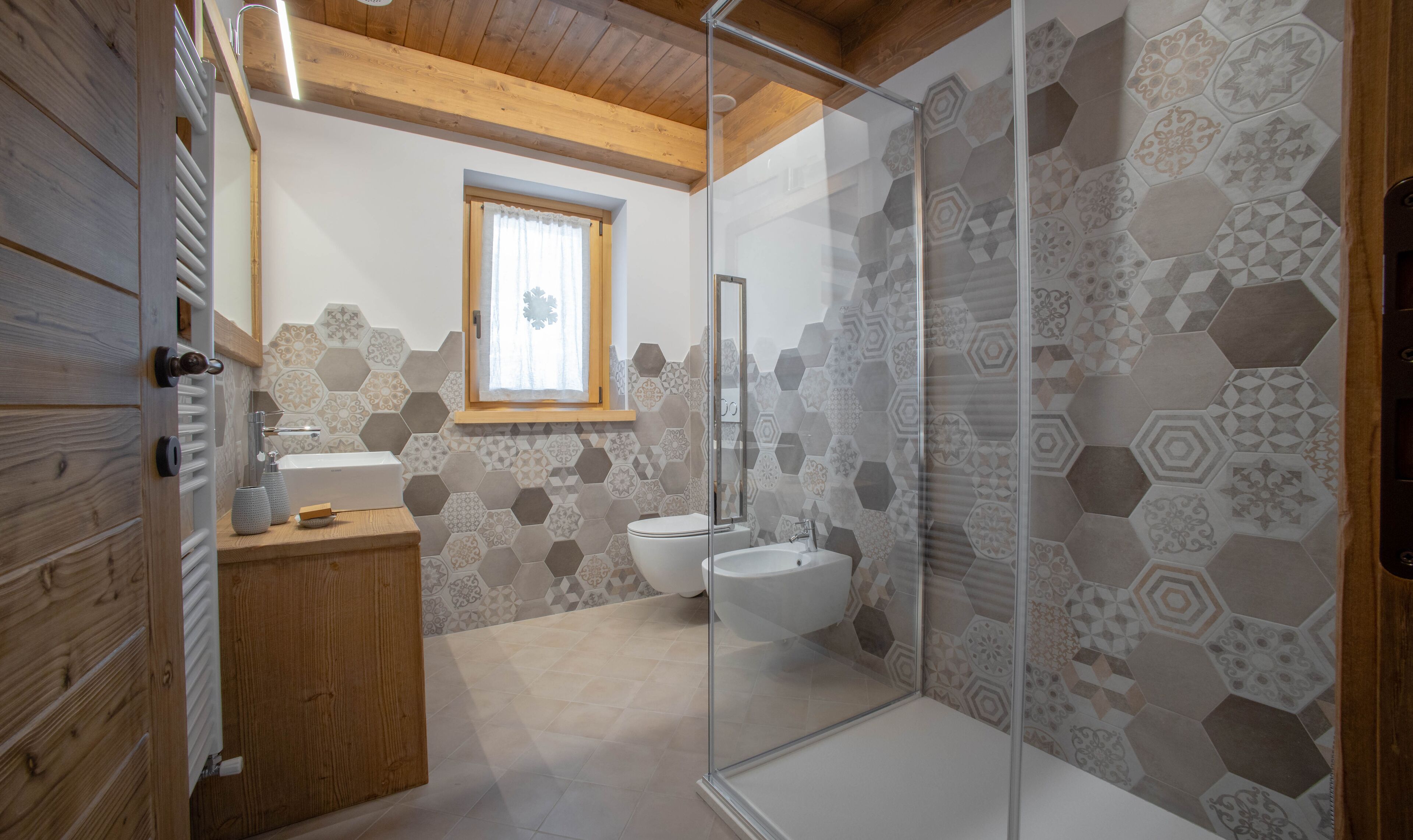 Et moderne badeværelse med en glasvægs brusekabine, et trækommode, toilet og et vindue med gardin.