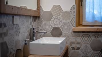 Un baño con un lavamanos rectangular, encimera de madera y un espejo encima. La pared presenta un diseño geométrico de azulejos.