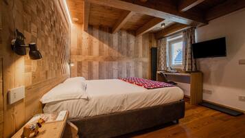 Ein Schlafzimmer mit Holzbalkendecke, einem Bett mit weißer Bettwäsche, einem Schreibtisch mit Computer und einem an der Wand befestigten Fernseher.