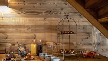 A wooden interior with a breakfast setup including jars of jam, honey, and a fruit bowl.