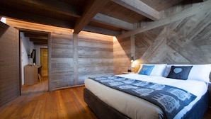 Een slaapkamer met een houten plafond, een bed met beddengoed met een patroon, en een houten vloer.