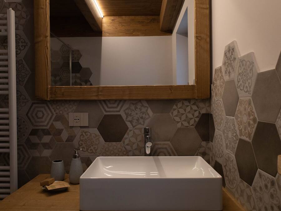 Un baño con un lavamanos rectangular, un mueble de tocador de madera, un espejo y baldosas hexagonales en las paredes.