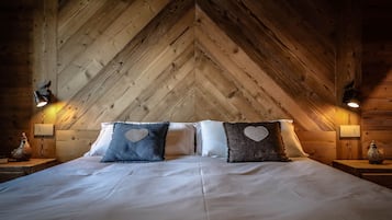 Een gezellige slaapkamer met een houten plafond, een bed met witte lakens en hartvormige kussens.