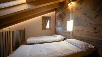 Un dormitorio acogedor en el desván, con dos camas, vigas de madera, techo inclinado y un ventanal con cortinas.