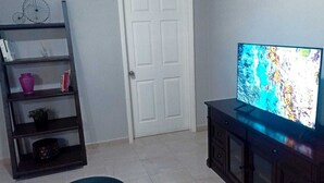 A room with a TV on a stand, a bookshelf with various items, and a closed door. - Exclusive apartment in Mxl 3 (Mexicali)