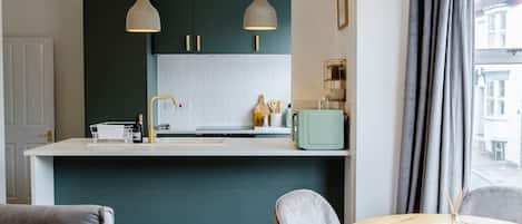 Una cocina moderna con encimera blanca, dos lámparas colgantes y un salpicadero color turquesa.