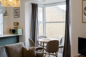 A cozy living area with a sofa, a table, chairs, a television, and a window with curtains.