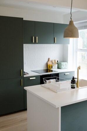 A modern kitchen with dark green cabinets, a white countertop, and a pendant light. - Relaxed Coastal Living – Stylish 1-Bedroom Apartment Just Minutes from Margate Beach (Kent)
