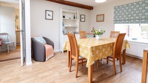 A dining area with a table set for four, wooden chairs, a yellow tablecloth, and a vase with flowers.