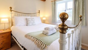 A neatly made bed with white linens, a green throw blanket, and a wooden nightstand with a lamp.