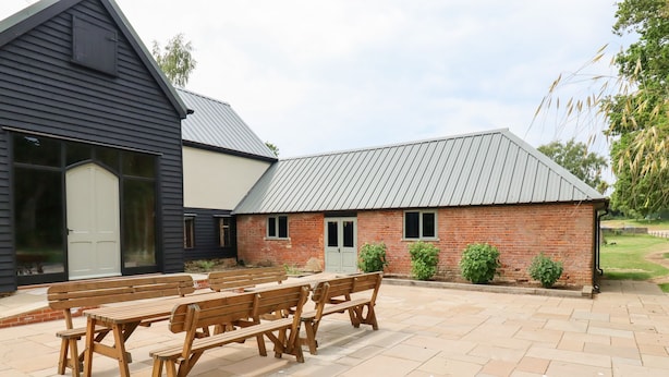 A patio with wooden benches and a brick building with a metal roof.