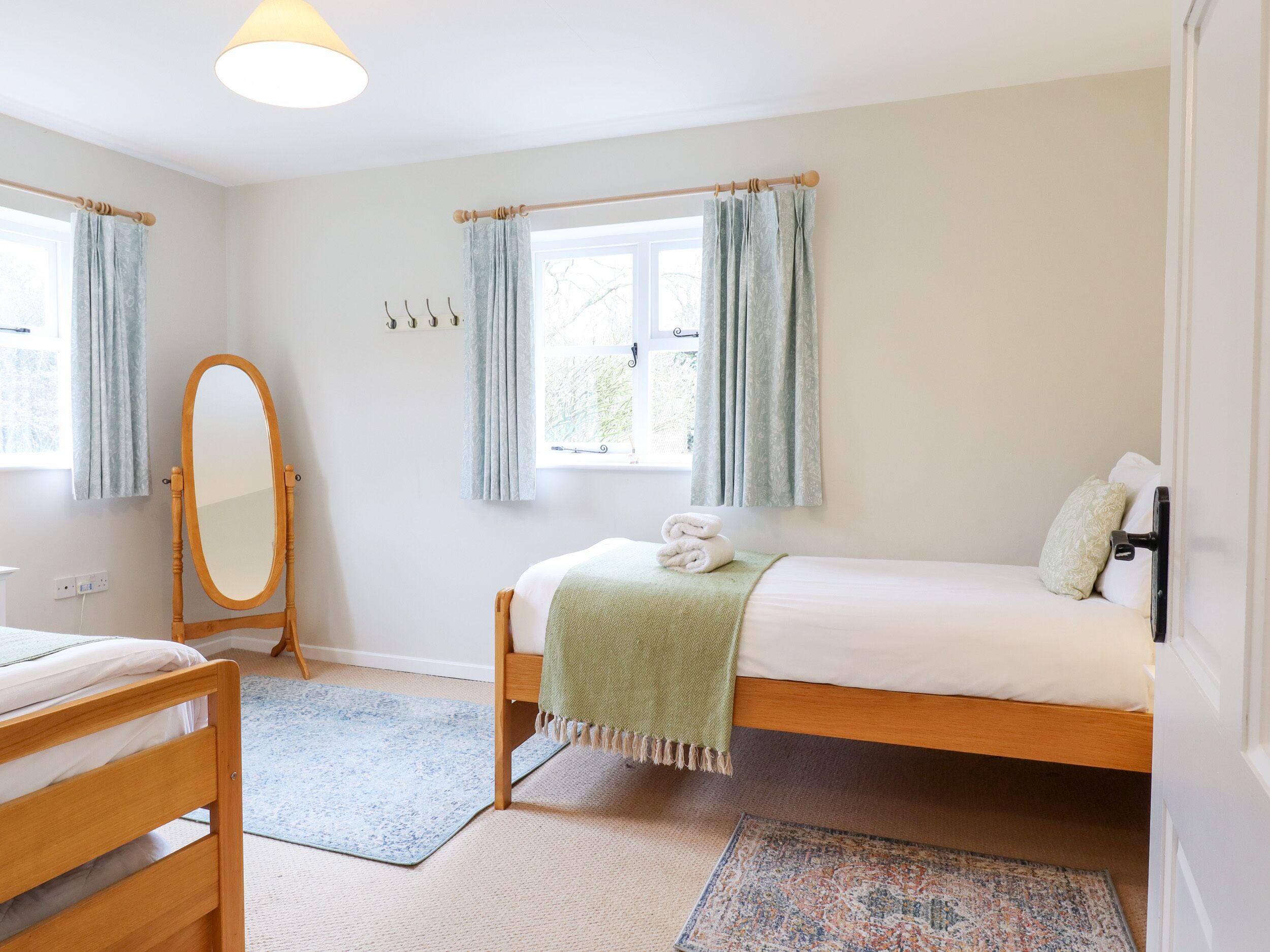A bedroom with a single bed, a wooden dresser, a mirror, and a window with curtains.