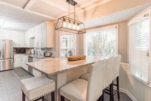 Una cocina moderna con armarios blancos, una isla central con asientos y una lámpara colgante.