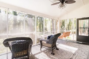 Una habitación soleada con ventanas amplias, sillas de mimbre y un tapete estampado.