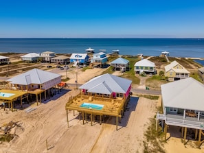 Vista aérea de uma área residencial costeira com casas sobre pilares, uma praia e o oceano ao fundo.