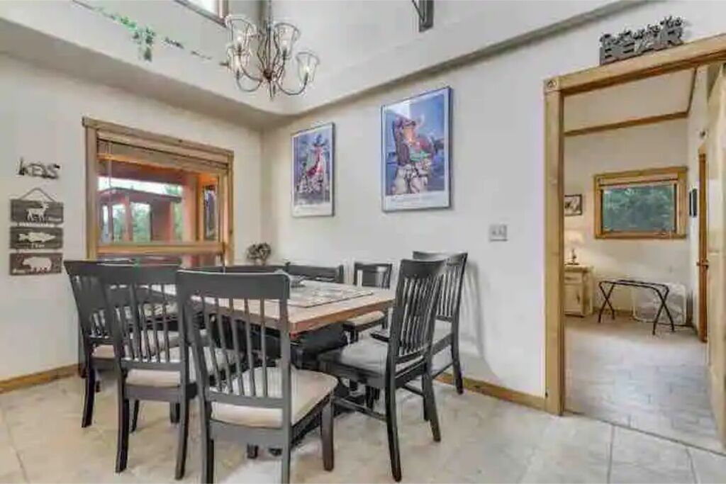 A dining area with a wooden table and chairs, framed pictures on the walls, and a chandelier.
