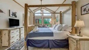 A bedroom with a large bed, a television, and a window with a view of greenery. - Remote Cabin Family Fun Hot Tub (Florissant)