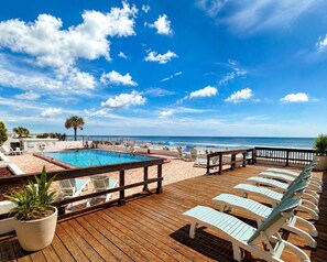 A wooden deck with a pool, lounge chairs, and a view of the ocean.