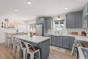 A modern kitchen with grey cabinets, a large island, and a dining area with white chairs.